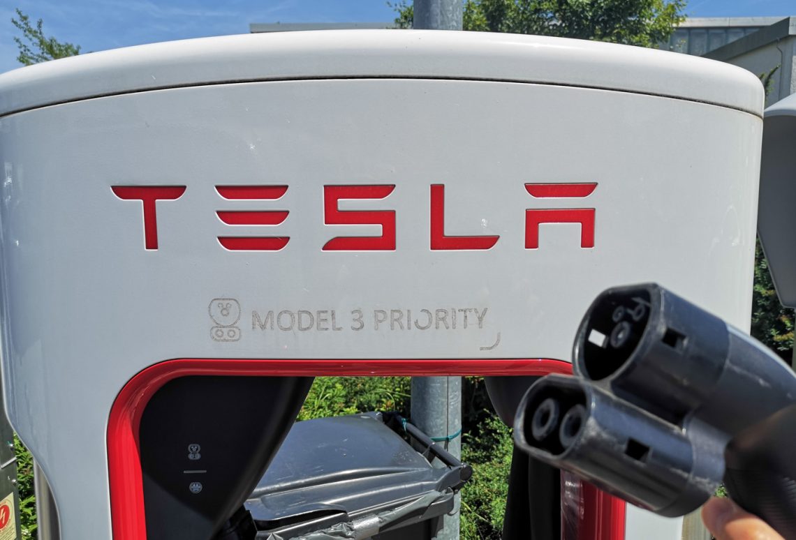 CCS-Ladekabel vor einer Tesla-Supercharger-Ladesäule