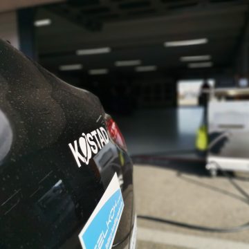 Details der KArosserie des BMW i4 mit dem Kostad-Schriftzug. Im Hintergrund eine Ladestation.
